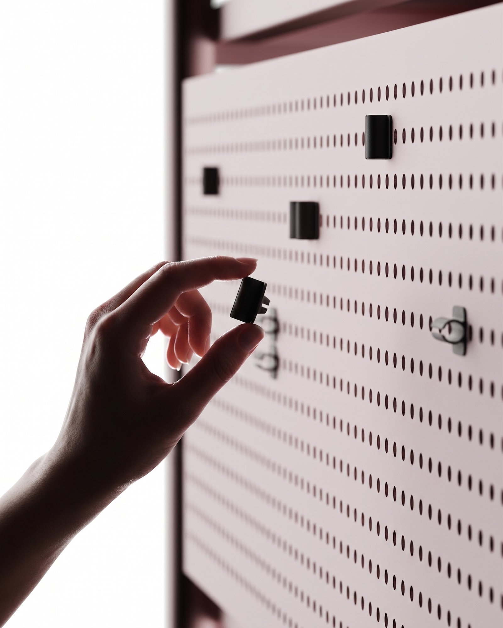 Détail du système de cable management du meuble vinyle Lara par Alix Videlier. Une main ajuste un insert en plastique noir sur le panneau arrière perforé pour organiser un câble audio.